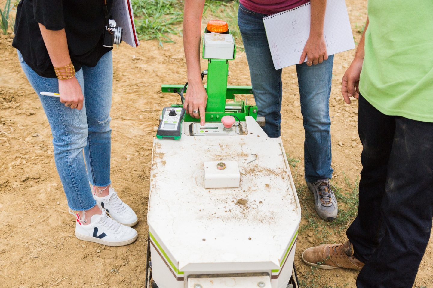 Gros plan sur le pupitre de commande d'un robot agricole Naïo, avec une utilisatrice actionnant les boutons pendant que d'autres personnes observent